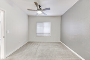 Interior Unit Bedroom, Ceiling fan/light fixture, window on left wall when entering, neutral toned walls and carpeting, darker painter wall right of window.