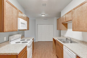Interior Unit Kitchen, Light brown cabinetry, double stainless steel sink, white appliances, storage with washer and dryer hookups parallel to kitchen, wood like floors, laminate countertops.