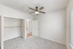 Interior Unit Bedroom, Folding closet doors, Ceiling fan/light fixture, neutral toned wall paint and carpeting, window opposite of bedroom door.