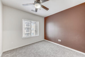 Interior Unit Bedroom, White wall with double window, ceiling fan/light fixture, neutral toned carpeting, terracotta toned wall right of window.