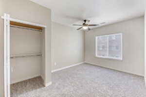 Interior Unit Bedroom, Walk in closet, ceiling fan/light fixture, neutral toned wall paint and carpeting, window on far side wall.
